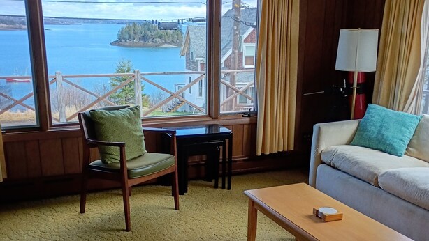 Ein Zimmer mit einer Couch, einem Sessel, einem kleinen Tisch und Seeblick durch große Fenster.