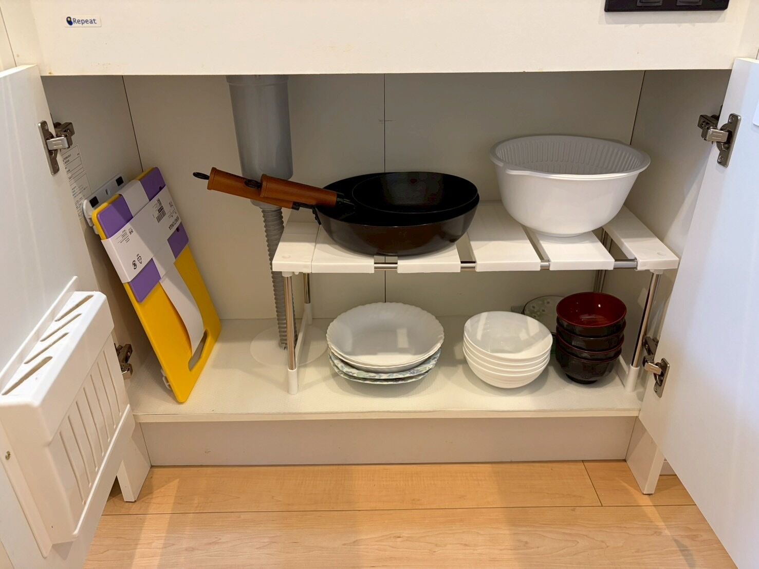 A kitchen with white cabinets, a white countertop, a black frying pan, a white bowl, and stacked white plates.