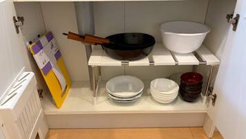 A kitchen with white cabinets, a white countertop, a black frying pan, a white bowl, and stacked white plates.
