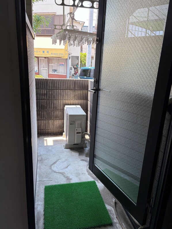 A doorway leading to a courtyard with a green mat, a white heater, and a wooden fence.