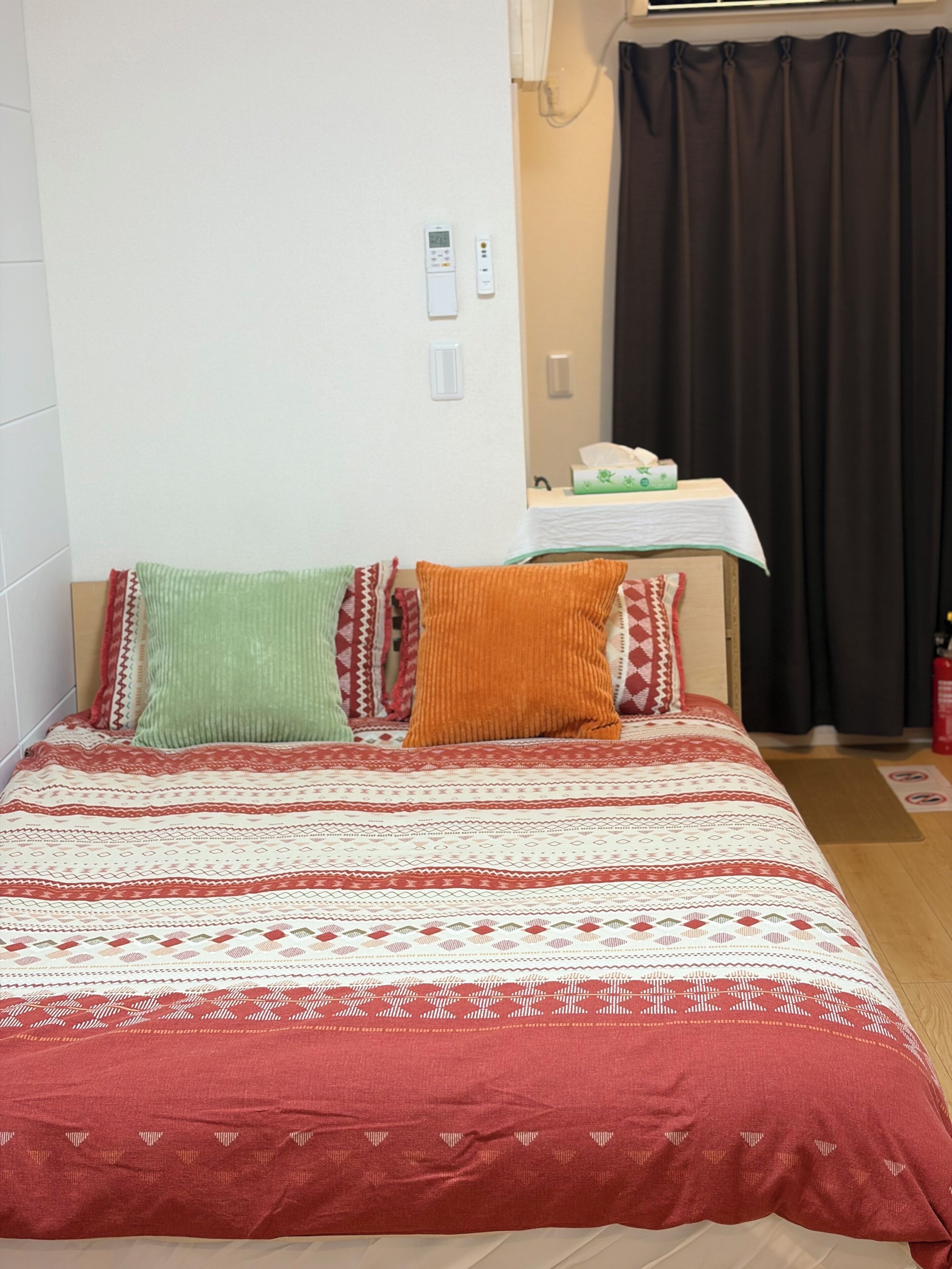 A bed with a patterned bedspread, pillows, a bedside table with a tissue box, and a window with curtains.