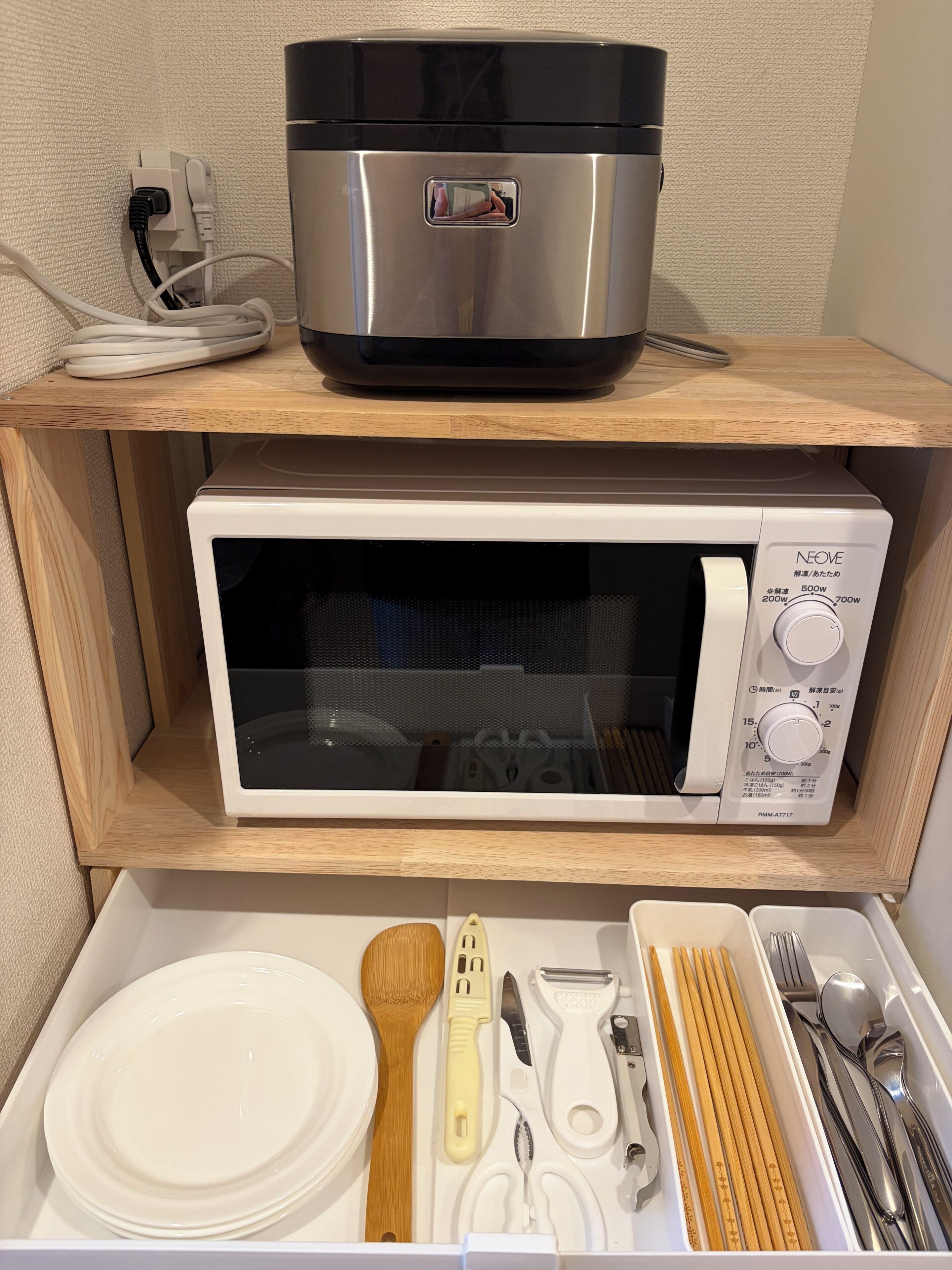 A microwave and a rice cooker on a shelf, with a drawer below containing kitchen utensils.