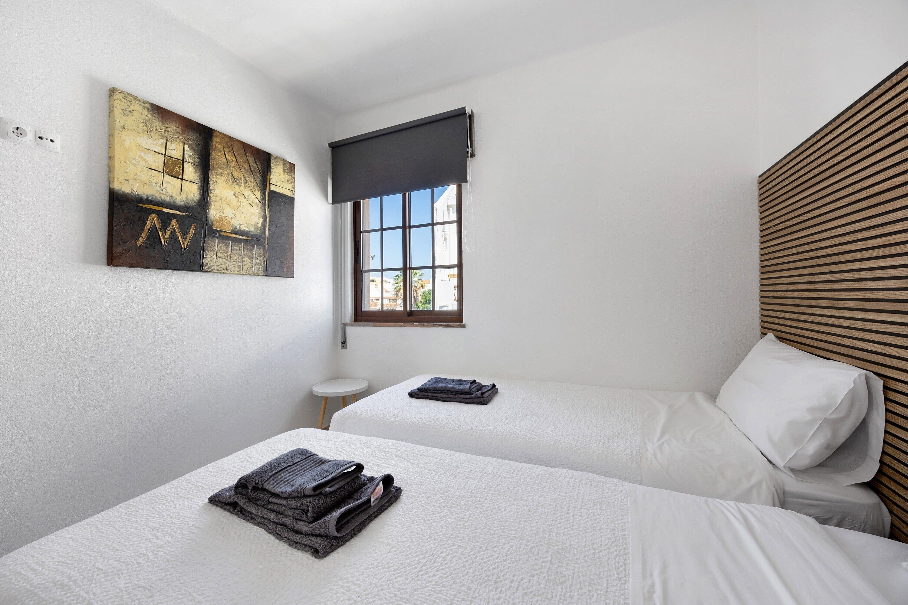 Een hotelkamer met twee bedden, een raam, een schilderij en een houten hoofdbord.