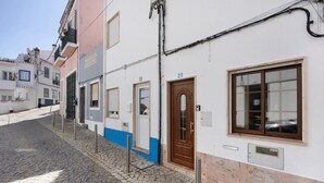 En kullerstensgata med byggnader som uppvisar traditionell arkitektur, inklusive en framträdande dörr och ett fönster med en nummerskylt.