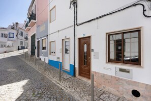 Una strada acciottolata fiancheggiata da edifici dall'architettura tradizionale, con una porta e una finestra in evidenza, complete di targa con il numero civico.
