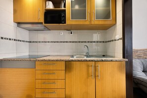 Una cocina compacta con armarios de madera, un lavamanos de acero inoxidable y un microondas.