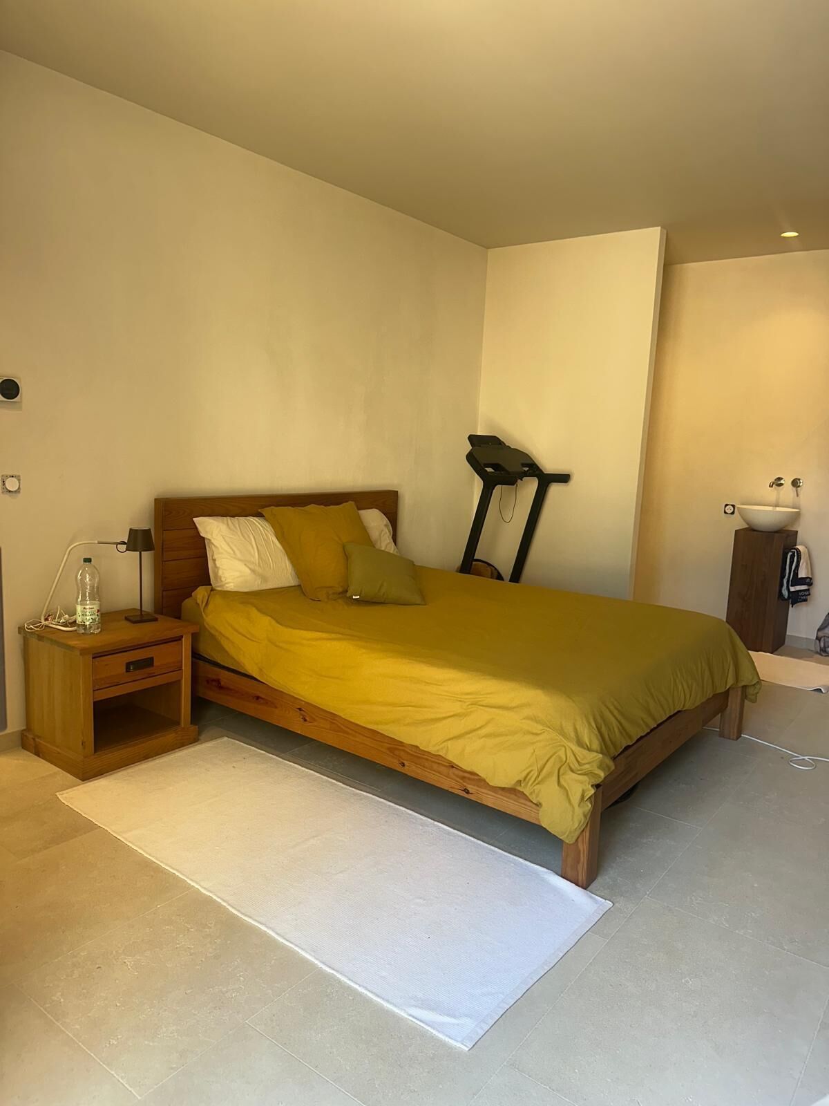 A bedroom with a bed, bedside table, lamp, and a small wooden cabinet.