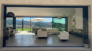 Un'ampia zona giorno con una grande vetrata scorrevole che dà su un balcone, arredata con divani bianchi e un tavolo da pranzo.