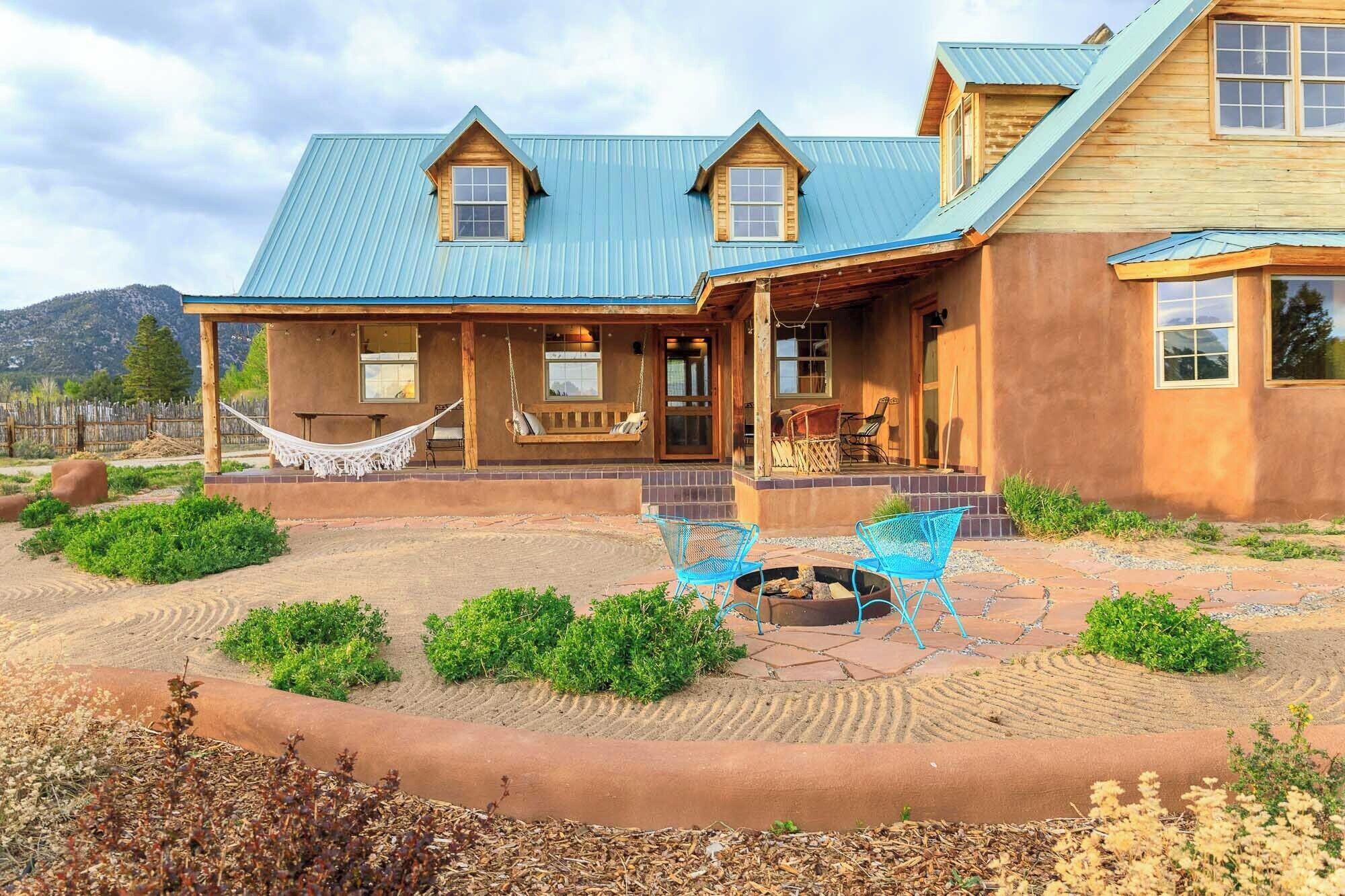 A rustic cabin with a covered porch, a hammock, outdoor seating, and a fire pit.