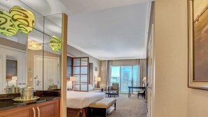 Ett hotellrum med en säng, ett sängbord, en lampa, en stol och ett stort fönster med utsikt över staden.