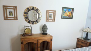 Een kamer met een houten kast, een spiegel, een Boeddhabeeldje, een ingelijst schilderij en een lamp.