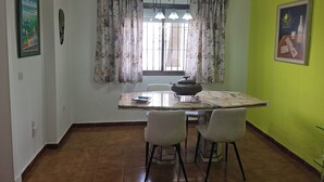 Een eethoek met een tafel, stoelen, een raam met gordijnen en een groene wand.