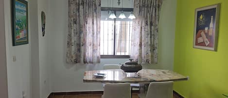 A dining area with a table, chairs, a window with curtains, and a green wall.