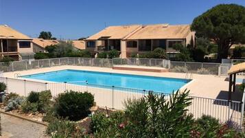 Une piscine entourée d’une clôture, avec des bâtiments adjacents et de la verdure.