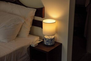 Een bed met witte lakens, een nachtkastje met een lamp en een afstandsbediening op het tafeltje.