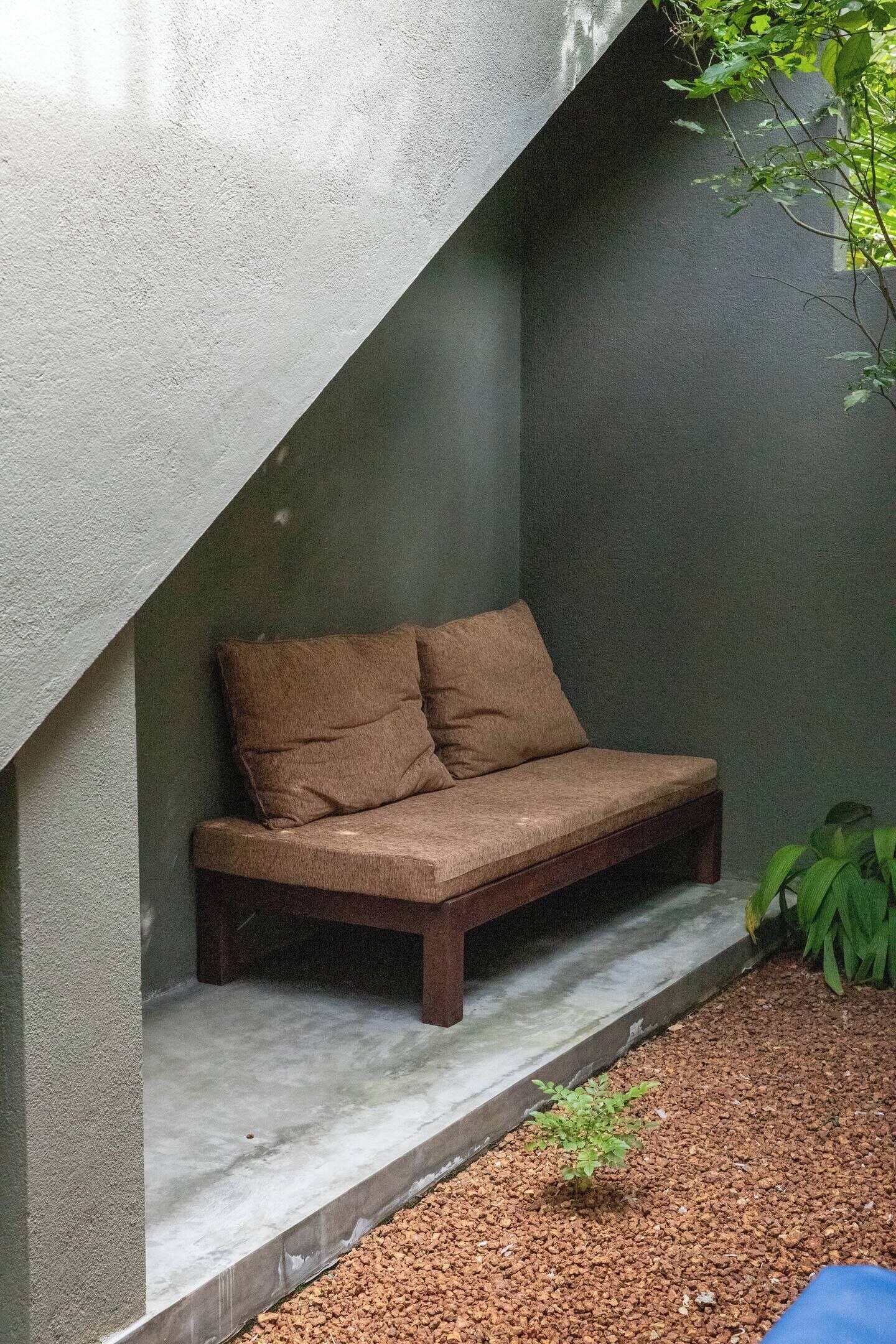 A corner seating area with a bench and cushions, a small plant, and a pebble-covered ground.