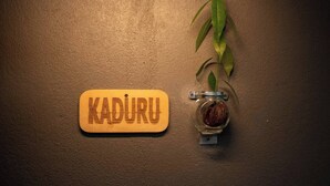 A wooden plaque with the word 'KADURU' and a glass jar with a plant on a textured wall. - Crystal Green Beach Villa – Villa 3 (Kuligoda)