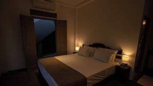 A bedroom with a bed, bedside lamps, a wooden door, and an air conditioning unit. - Crystal Green Beach Villa – Villa 3 (Kuligoda)