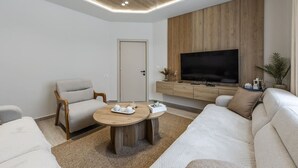 A modern living room with a sofa, armchair, coffee table, TV, and wooden panel wall. - Loen Modern Seaside 3BR Apartment by PikHost (Durrës)