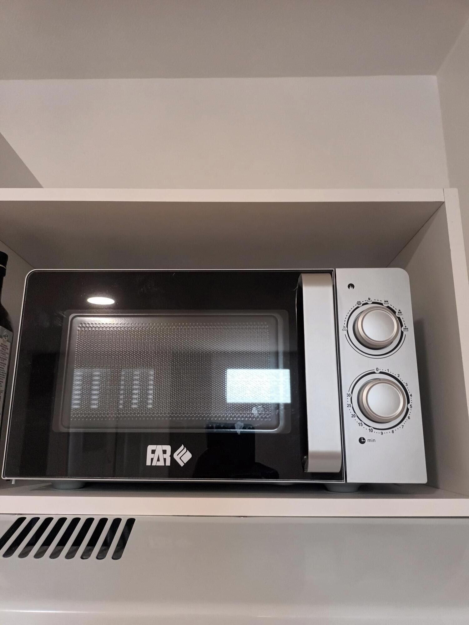 A microwave oven with two dials, placed on a white shelf.