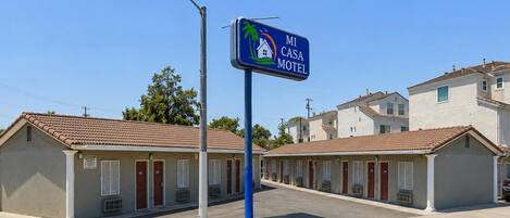 A motel with a sign indicating 'MI CASA MOTEL,' featuring a house and palm tree logo.