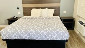 A bed with a patterned bedspread, two bedside tables, a wall-mounted phone, and a window with blinds.