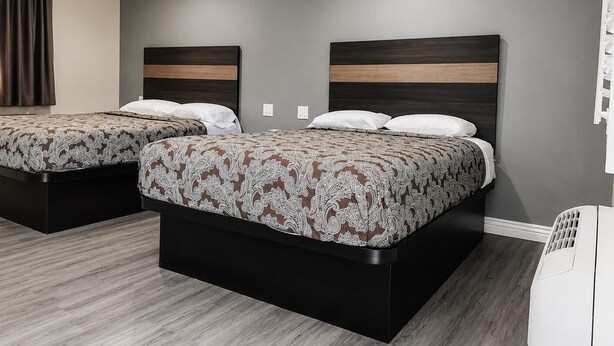 A hotel room with two beds, a grey wall, and a white air conditioning unit.