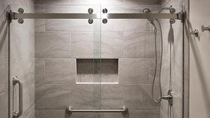 A modern shower stall with a glass door, grab bars, and a handheld showerhead.