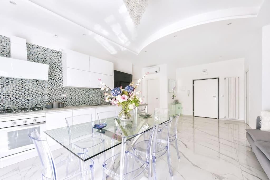 Una cucina moderna con un tavolo da pranzo in vetro, pensili bianchi e un'elegante composizione floreale.