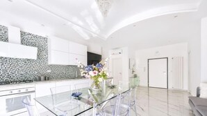 Una cocina moderna con una mesa de comedor de vidrio, armarios blancos y un arreglo floral decorativo.