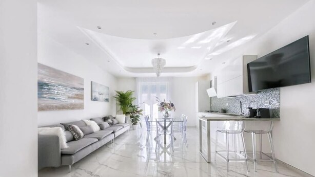 Un espacio habitable moderno con sofá, mesa de comedor, sillas y televisor montado en la pared.
