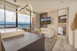 A modern living room with a large window, a sofa, a coffee table, and a dining area.
