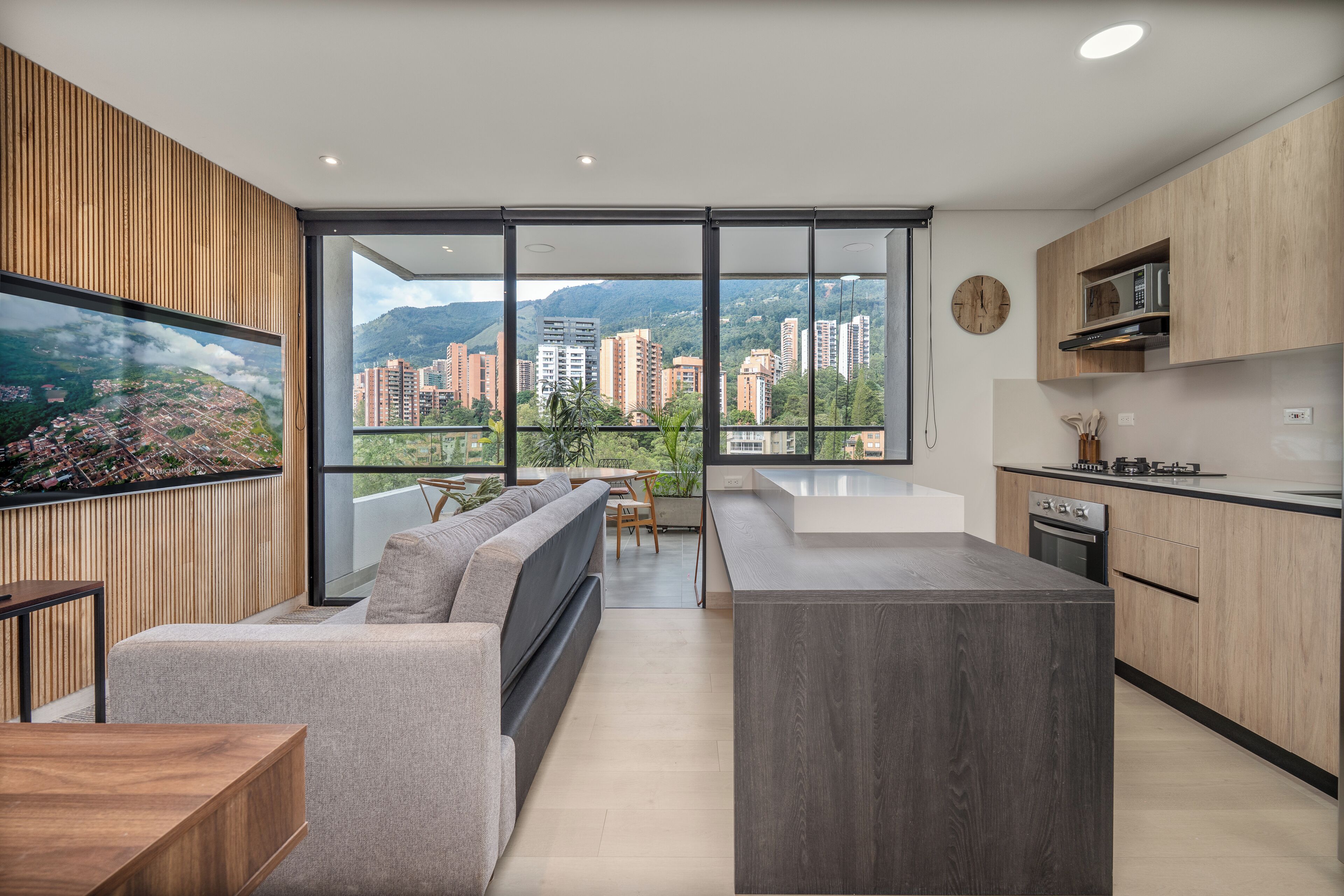 A modern kitchen with a large island, a dining area with a sofa, and a view of a cityscape through large windows.