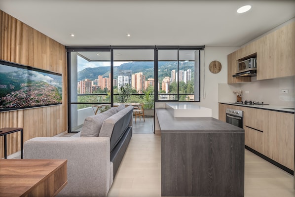 A modern kitchen with a large island, a dining area with a sofa, and a view of a cityscape through large windows.