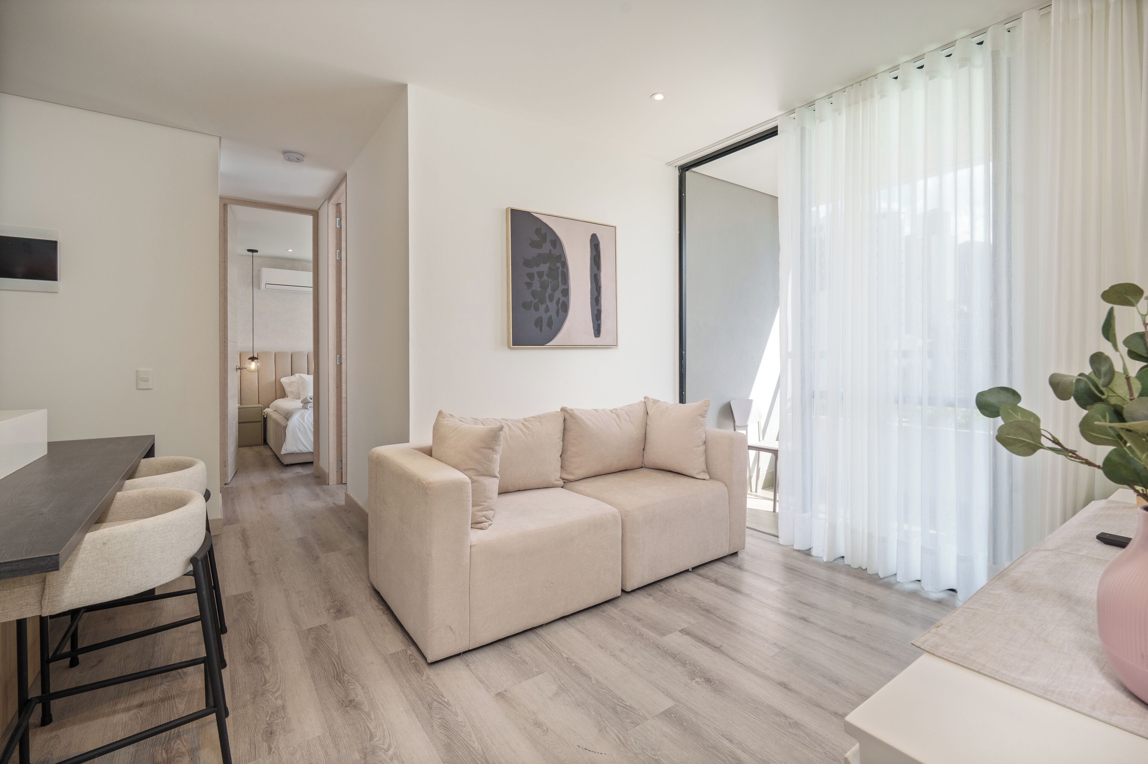 Un salon moderne avec un canapé, un coin repas comprenant une table et des chaises, et une grande fenêtre ornée de rideaux légers.