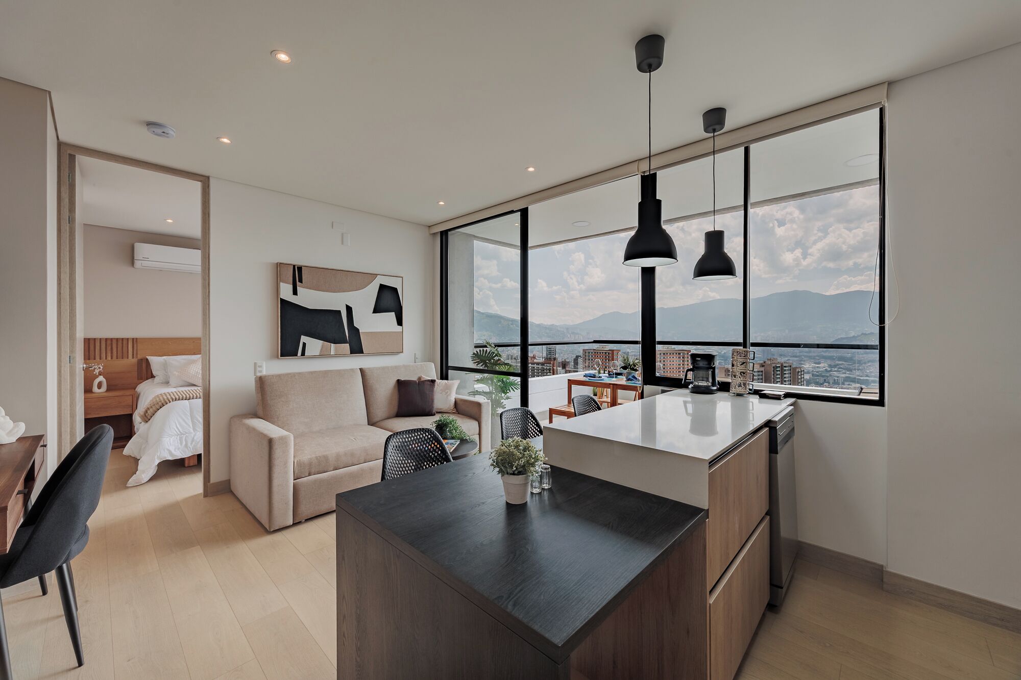 A modern living room with a large window, a sofa, a dining area, and a kitchen island.