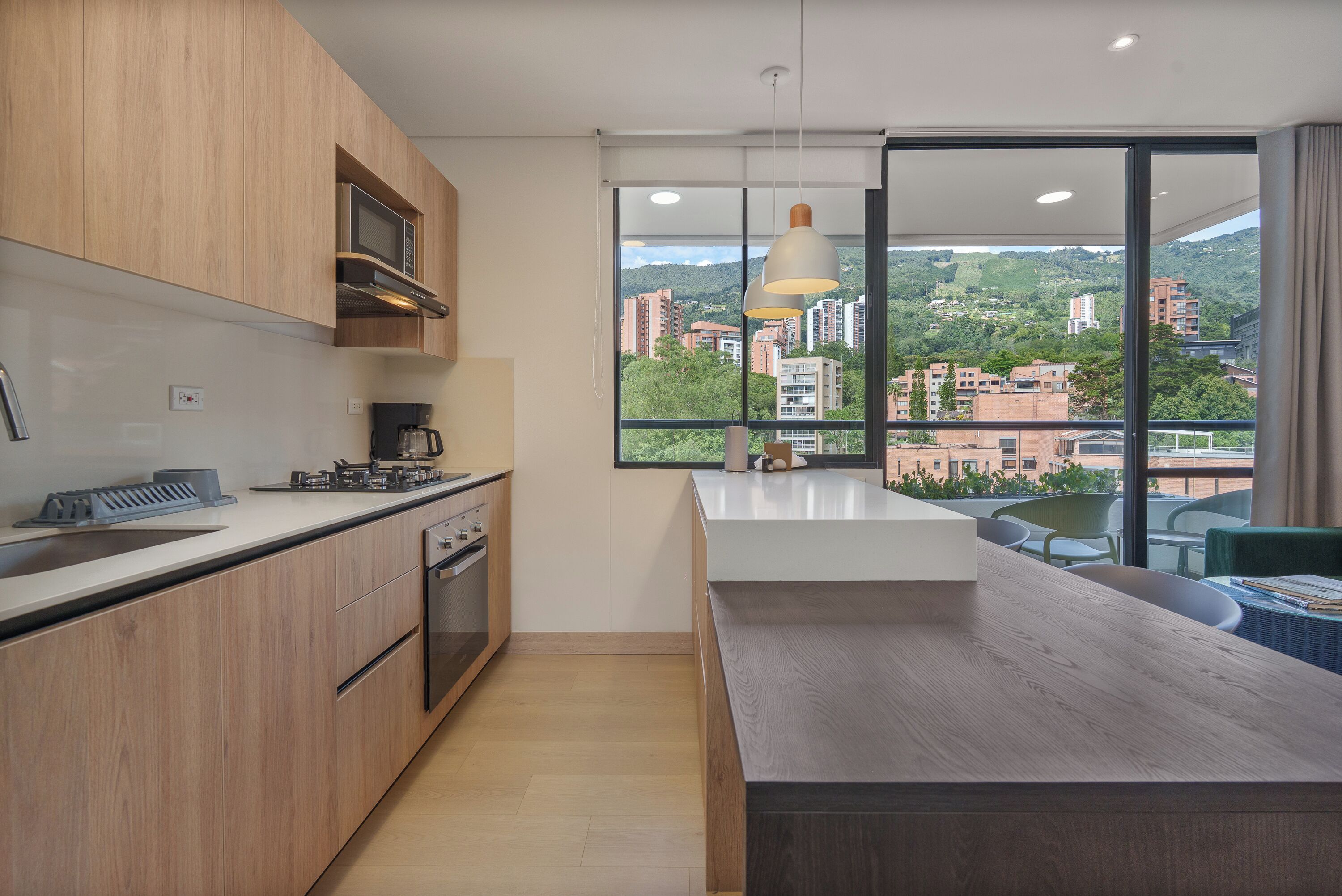 A modern kitchen with wooden cabinets, a built-in microwave, and a large window offering a city view.