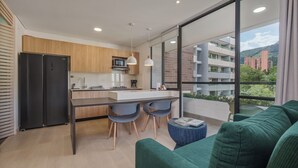 A modern kitchen with a dining area, large windows, and a green sofa. - GRAND BY LINARES  (Medellín)