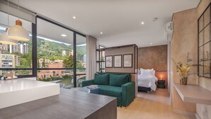 A modern hotel room with a large window, a green sofa, a bed, and a desk area. - GRAND BY LINARES  (Medellín)