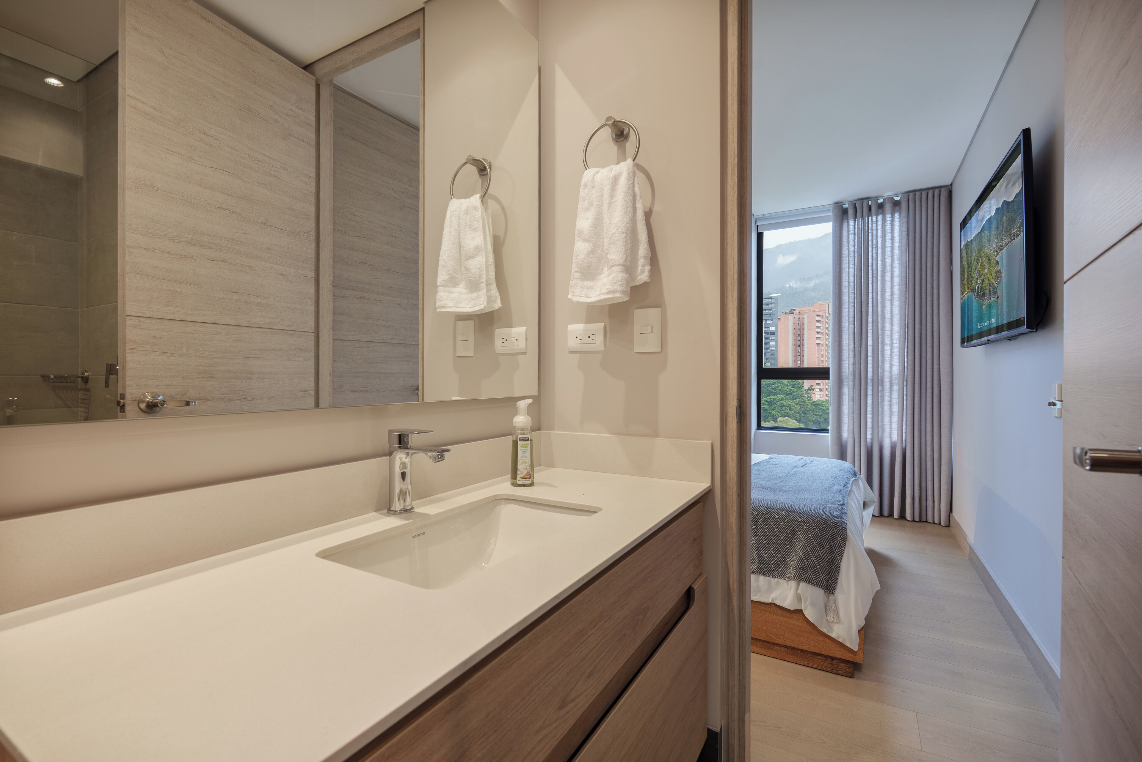 A modern bathroom with a large mirror, two towel rings, a sink, and a shower.