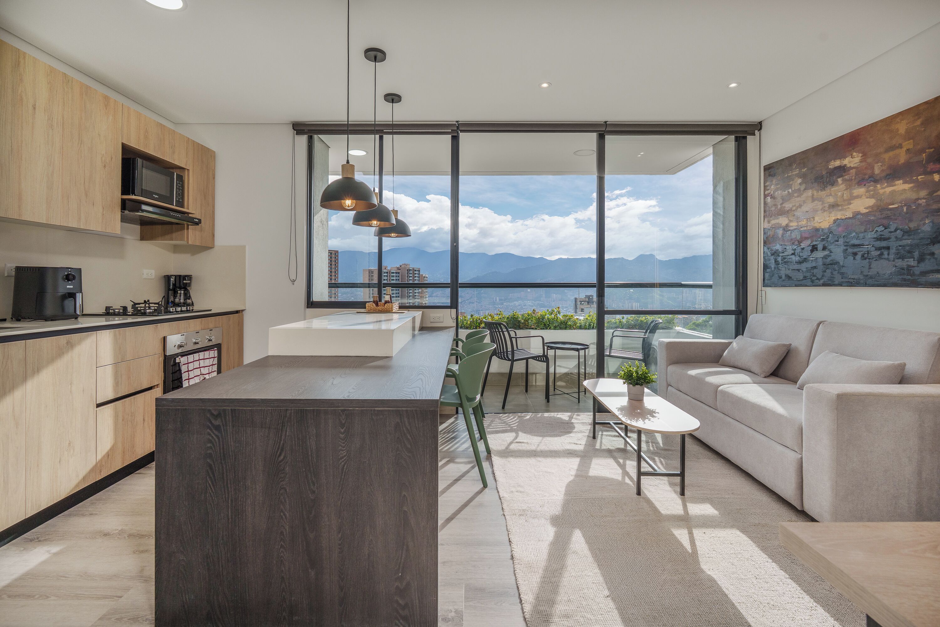 A modern kitchen with a central island, a dining area with a view, and a living space with a sofa and a painting.