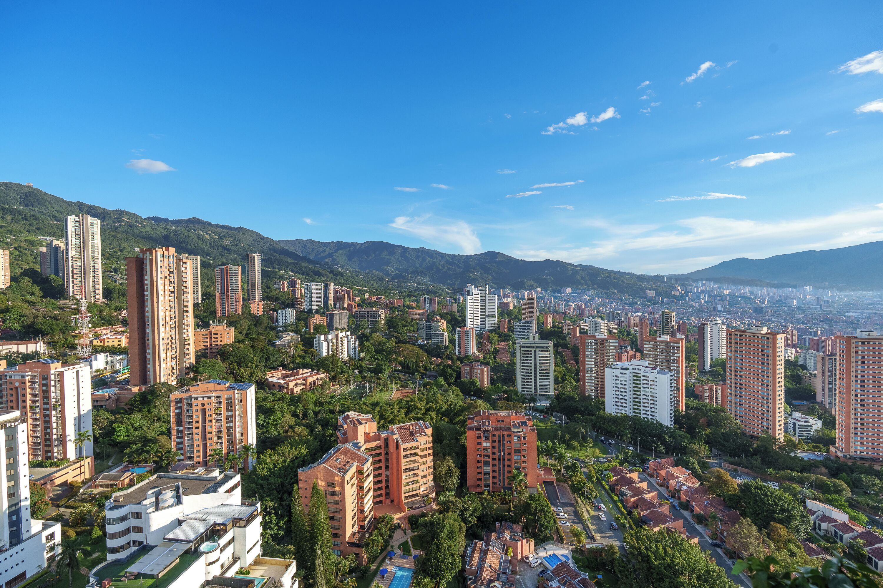 Un paisaje urbano con rascacielos, una combinación de edificios residenciales y comerciales, y montañas al fondo.