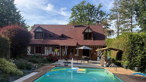 Una casa con piscina, un patio con mobiliario exterior y un jardín.