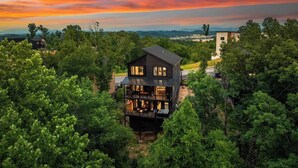 Une maison à plusieurs étages, entourée d’arbres, qui offre une vue sur les montagnes lointaines.