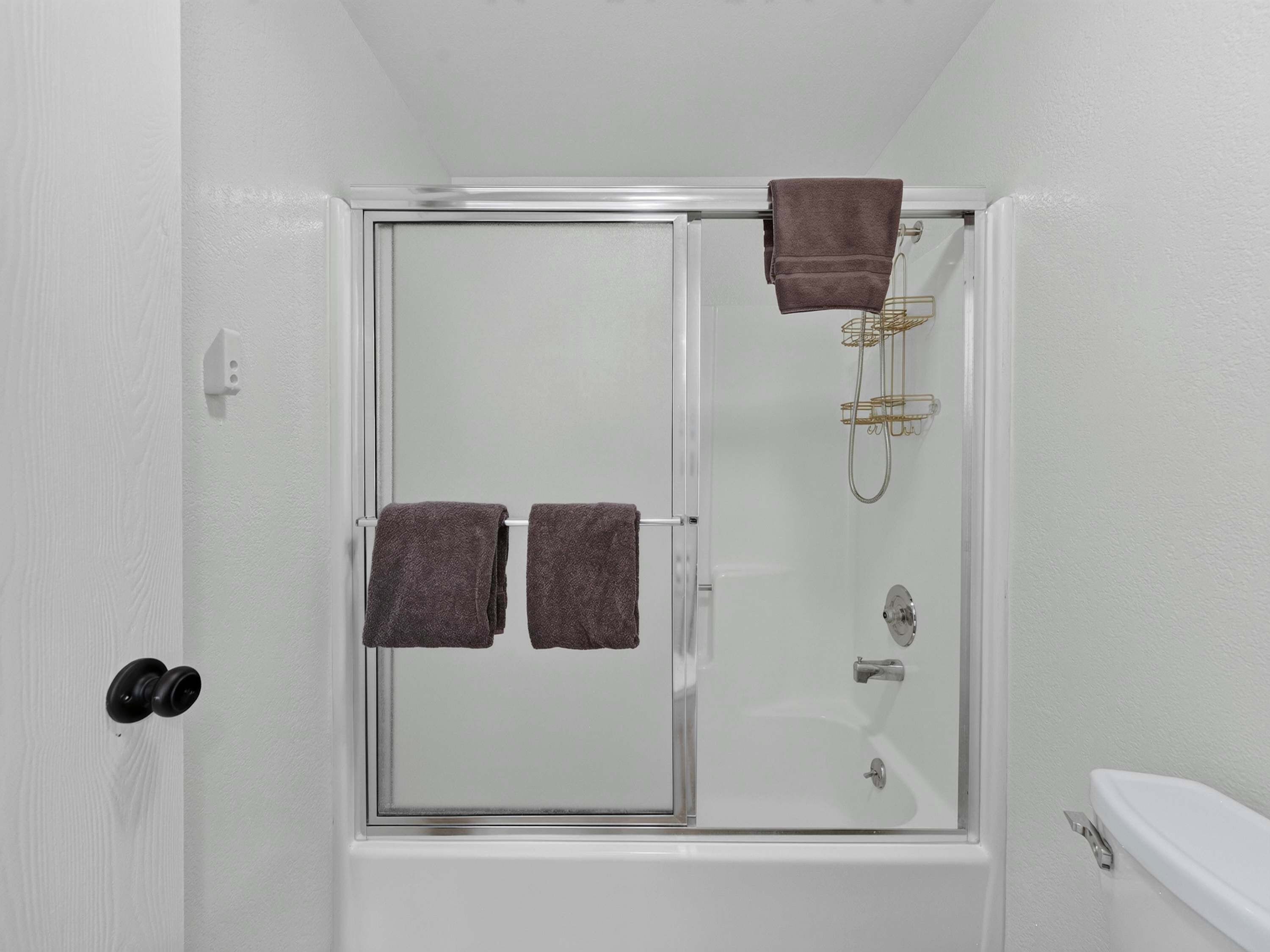 Un bagno con cabina doccia in vetro, due asciugamani appesi al muro, un water e un soffione.