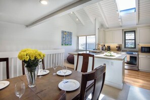 Een moderne keuken met witte kastjes, een centraal eiland en een eethoek met een houten tafel en stoelen.