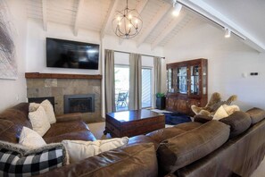 Ein Wohnzimmer mit Kamin, Ledersofas, einem Holzkasten und einem an der Wand befestigten Fernseher.
