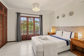 A bedroom with a bed, curtains, a wooden headboard, a nightstand, a bedside table, and a window with a view. - Villa 'Mabelle' with Sea View, Wi-Fi and Air Conditioning (Albufeira)