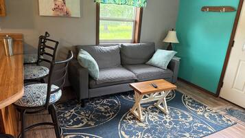 A cozy living area with a sofa, chairs, a small table, a window with a view, and a door.