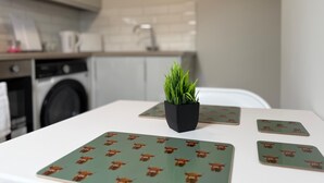 A kitchen with a table set with four square placemats featuring a pattern of brown animals, a small potted plant, and a white countertop. - Walk to Train Bolton ~Free Parking ~close to Shops (Farnworth)